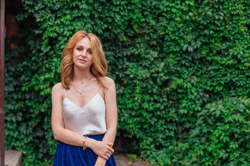 Portrait of a young beautiful woman, standing next to the wall of wild grape leaves.