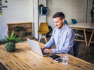 concentrating and  typing remote online working man in casual outfit with laptop, mobile, glass and...