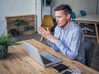 happy smiling remote online working man having his hand up with laptop and notebook in casual...