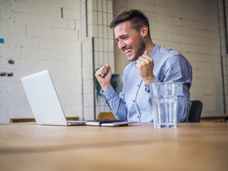happy smiling remote online working man in casual outfit with laptop in joyful successful winning...