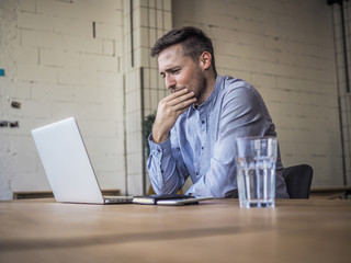thinking remote online working man having his hand on chin and looking at laptop in casual outfit...