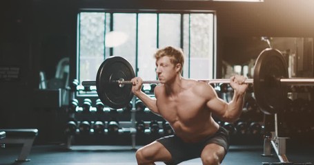 Strong muscular man working out doing barbell squats in the gym as part of his fitness routine, man with an amazing body sculpted by determination and focus