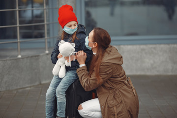 A European mother in a respirator with her daughter are standing near a building.The parent is...