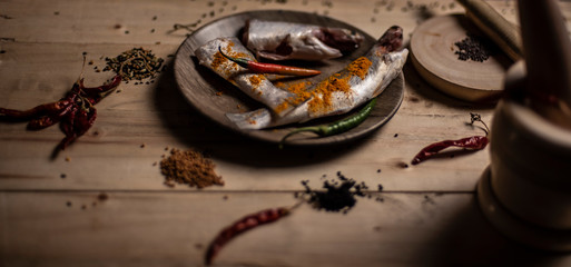 Top view of Indian fishes decorated with whole spices kept on a wooden dish on a wooden tray. Food photography.