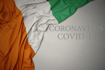 waving national flag of cote divoire on a gray background with text coronavirus covid-19 . concept.