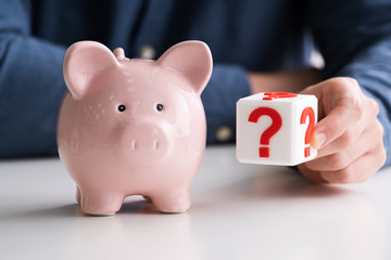 Man Holding Question Mark Next To Piggy Bank