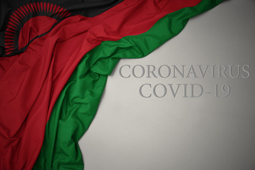 waving national flag of malawi on a gray background with text coronavirus covid-19 . concept.