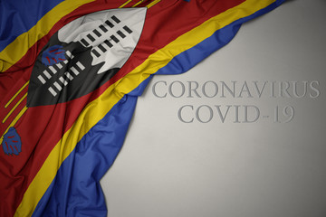 waving national flag of swaziland on a gray background with text coronavirus covid-19 . concept.