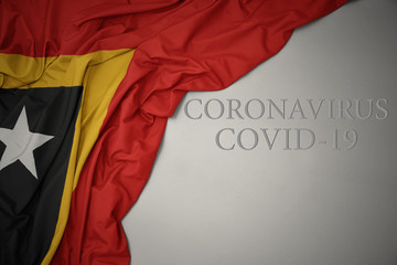 waving national flag of east timor on a gray background with text coronavirus covid-19 . concept.