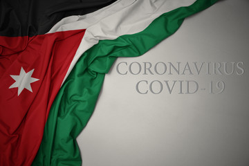 waving national flag of jordan on a gray background with text coronavirus covid-19 . concept.