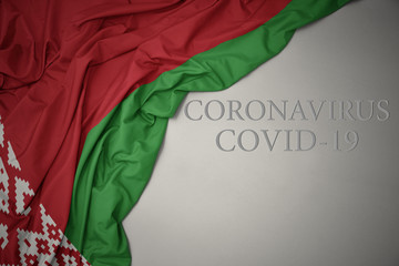 waving national flag of belarus on a gray background with text coronavirus covid-19 . concept.