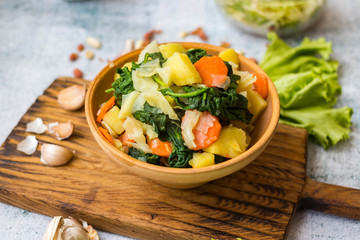 Cooked, steamed or boiled seasonal vegetables in clay ceramic brown bowl pot. Carrot, potato, spinach, cabbage. Vegan, vegetarian low fat diet
