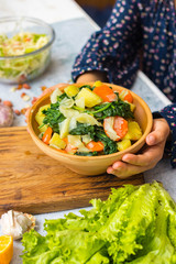 Cooked, steamed or boiled seasonal vegetables in clay ceramic brown bowl pot. Carrot, potato, spinach, cabbage. Vegan, vegetarian low fat diet. Holding hands