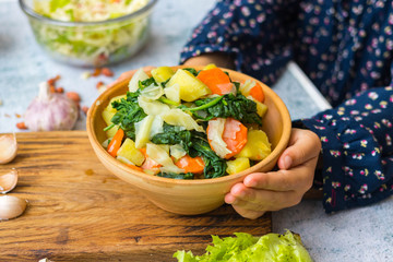 Cooked, steamed or boiled seasonal vegetables in clay ceramic brown bowl pot. Carrot, potato, spinach, cabbage. Vegan, vegetarian low fat diet. Holding hands
