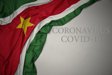 waving national flag of suriname on a gray background with text coronavirus covid-19 . concept.