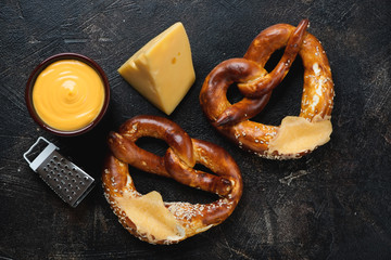 Two german pretzels with cheese dip on a dark brown stone background, horizontal shot, top view
