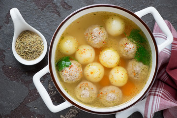 Soup with meatballs and potato balls served in a white bowl, top view on a brown stone background, horizontal shot