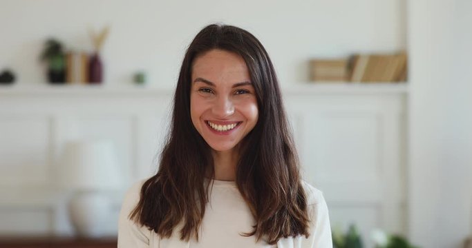 Cheerful pretty millennial woman looking at camera laughing with dental smile standing at home office indoors. Happy young beautiful lady close up portrait. White healthy teeth, dentistry concept