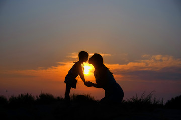 Silhouettes of mother and little daughter at sunset.