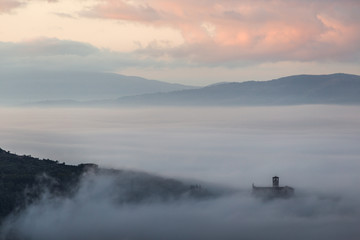 An epic view of St.Francis church in Assisi town (Umbria) above a sea of fog at dawn
