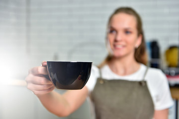 A young barista girl offers a large cup with coffee. Small business concept.