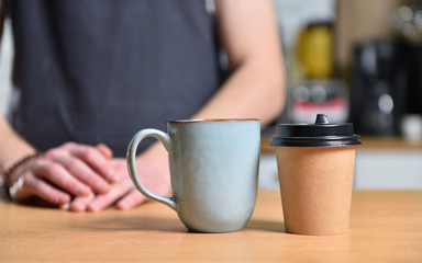 Paper cup of coffee and a mug on the table, against the background of a barista bartender guy. The concept of choice and alternatives