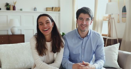 Happy young couple vloggers waving hands talking to camera streaming recording vlog at home. Smiling friends influencers shooting videoblog. Husband and wife making video call chatting. Webcam view - Powered by Adobe