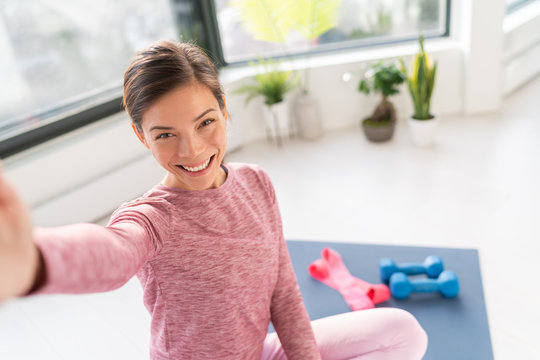 Happy selfie at home Asian young woman smiling training bodyweight exercises on exercise mat in living room of apartment taking mobile phone photo during workout.