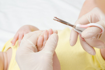 Hand in rubber protective gloves holding scissors. Cutting finger nails of infant. Closeup. Point of view shot.