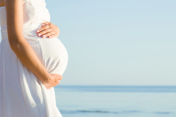 Young pregnant woman standing at sea beach. Sunny day. Emotional loving pregnancy time. Baby...