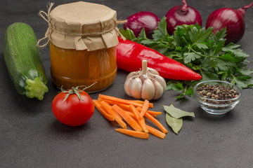 Canned squash spread in glass jar. Raw vegetables and spices: carrots garlic, onions tomatoes, star anise, chili peppercorn, parsley.