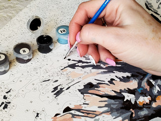 woman's hand draws a brush painting by numbers on the canvas.