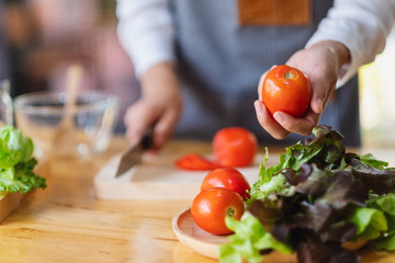 A woman chef holding and picking a fresh tomato from a vegetables tray on the table