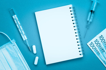 Notepad for copying space, thermometer, syringe, tablets and euro cash on a colored background.