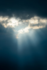 Dramatic sun rays breaking through the clouds on a very dark day, giving hope for the future.