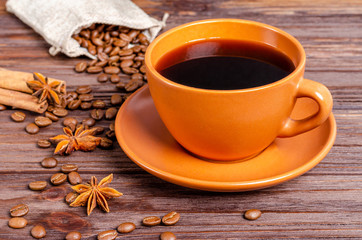 Cup of black aromatic coffee in a clay cup with anise stars and cinnamon sticks on a wooden background