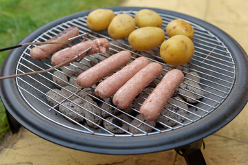 bbq grill cooking sausages and potatoes in backyard in england uk
