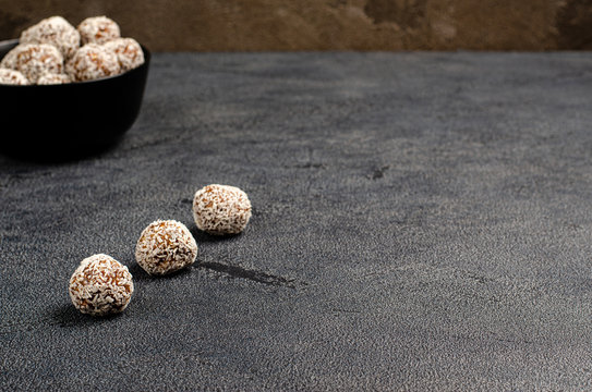 Homemade energy balls from dates, peanuts, oats, sprinkled with coconut in a black bowl on a dark background with copy space with place for your text