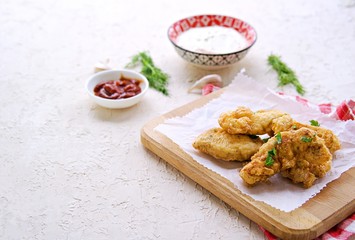 Chicken nuggets on a wooden board on a light concrete background. Served with ketchup and mayonnaise, yogurt and grainy mustard sauce. Food for parties. American cuisine. Copyspace