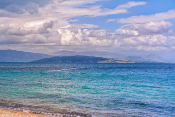 Beautiful landscape – turquoise colored sea water, golden sand, blue sky and white clouds and mountains on the horizon. 