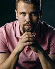 Fototapeta na wymiar Portrait of a young man with a beard in a pink polo t-shirt on a dark background