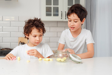 boys real brothers in a bright kitchen eating marshmellow from a glass jar