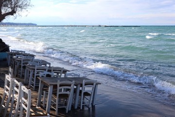 White chairs and tables on the beach. Windy day by the blue sea.