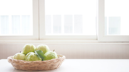 green guava (tropical fruit) with leaves with copy space are in a basket on white table background and near window, copy space.