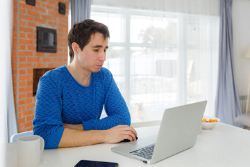 Fototapeta premium young attractive man freelancer working at home on a computer at the bright kitchen, stay at home