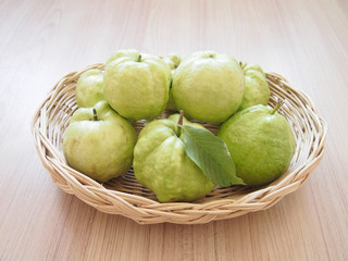 Green guava (tropical fruit) with leaves are in a basket on a wooden floor.