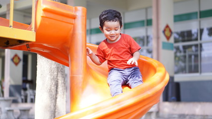Cute little Asian 2 year old toddler baby boy child playing on a slide at indoor playground in...