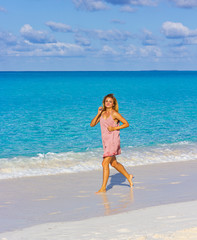Fototapeta premium Beautiful blonde runs along the beach. Smiling girl under the sun in a pink dress. Young slender woman on vacation.