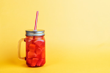 Glass jug with a tin lid and a red straw, with a cold drink made from pieces of fruit.