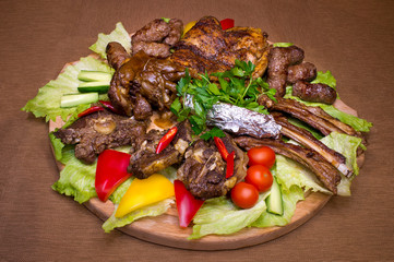Large meat baked set. Ribs, meat on the bone, fatty pieces of meat, chicken, cradles on the board with vegetables around